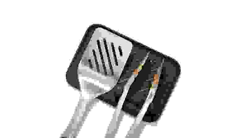 A set of grilling tongs and spatula resting on a small silicone mat.