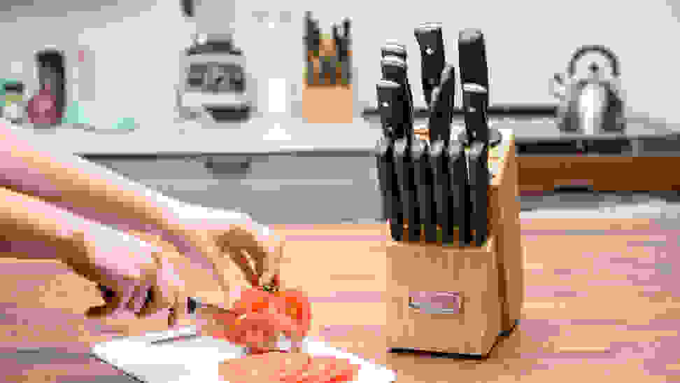 Close-up of a knife set and a hand model chopping a tomato.