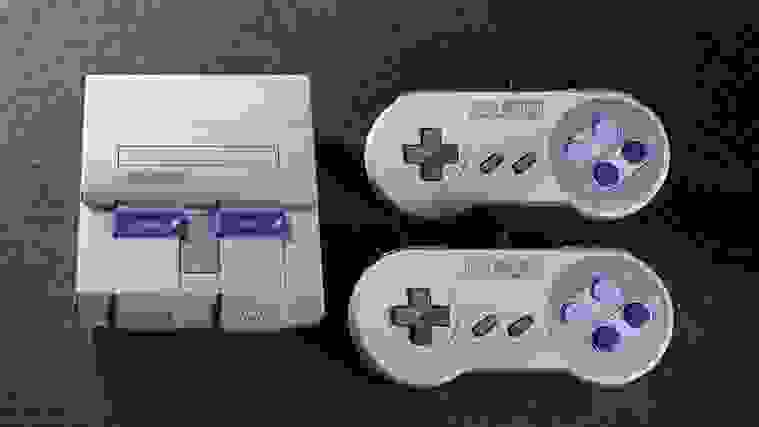 SNES console next to two controllers on grey textured background