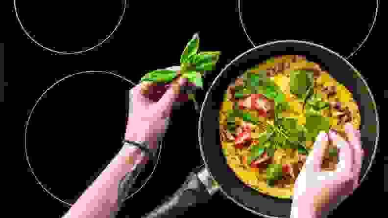 Two hands adding garnish to a frittata cooking on an induction cooktop