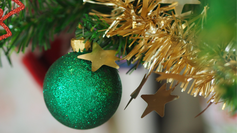 A green ornament hangs on a Christmas tree branch.