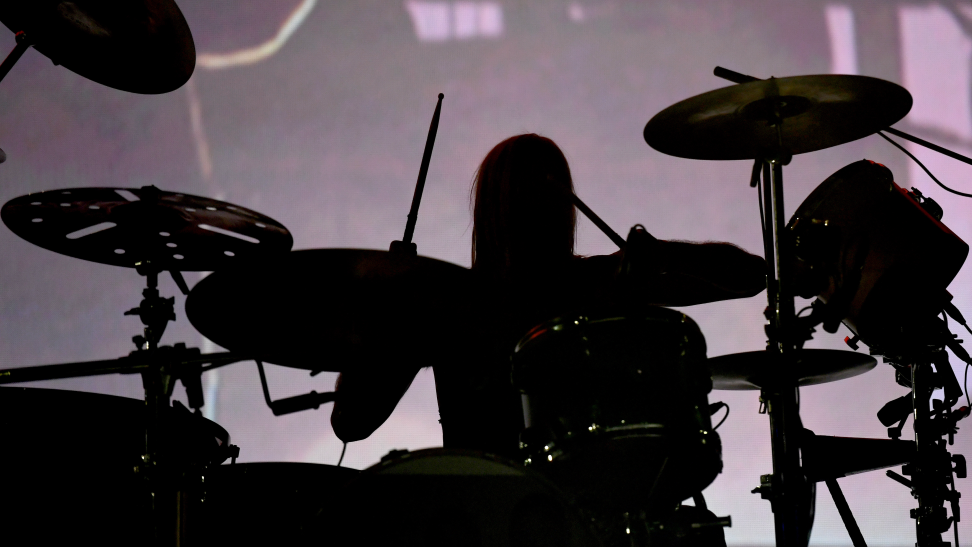Taylor Hawkins of the Foo Fighters sits behind a drum kit (in silhouette).