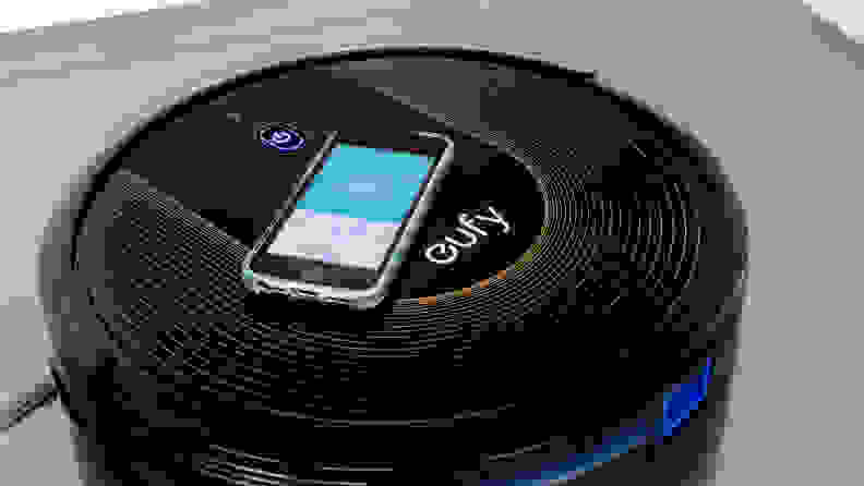 The Eufy Robovac 30C with a phone displaying its smart app atop it.