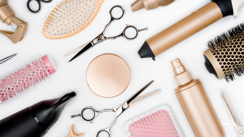 A flat lay image of several hair tools including shears, brushes, and a curling iron.