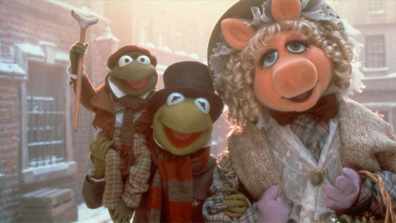 An ornately-dressed Miss Piggy (voiced by Frank Oz) and Kermit the Frog (voiced by Steve Whitmire) cary a Tiny Tim Cratchit frog (voiced by Jerry Nelson) down the cold city streets in 1992's The Muppet Christmas Carol