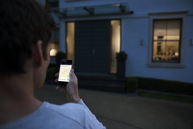 A man stands outside, operating his home's lights from his smartphone.