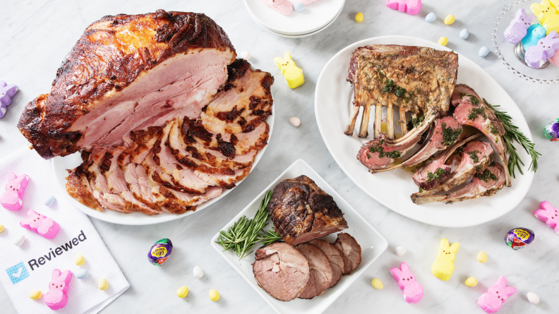 Cooked sliced ham, small lamb roast, and lamb chops on white plates are spread out on a white counter for serving.