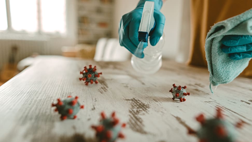 A person cleans a table with disinfectant and a rag. On the table is a model of coronavirus.