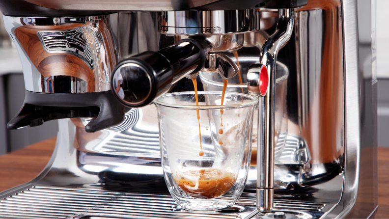 Cup of dark espresso being brewed into glass mug from the Breville Barista Touch Impress espresso machine.