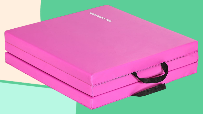 A folded pink yoga mat against green background.