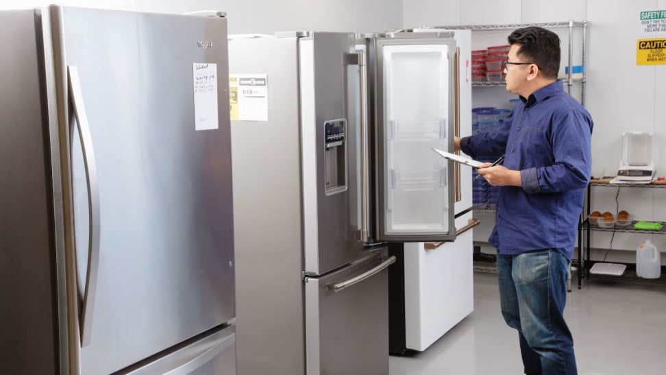 Person holding clipboard inspects the inside of a refrigerator while inside of a testing testing tab filled with other refrigerators.