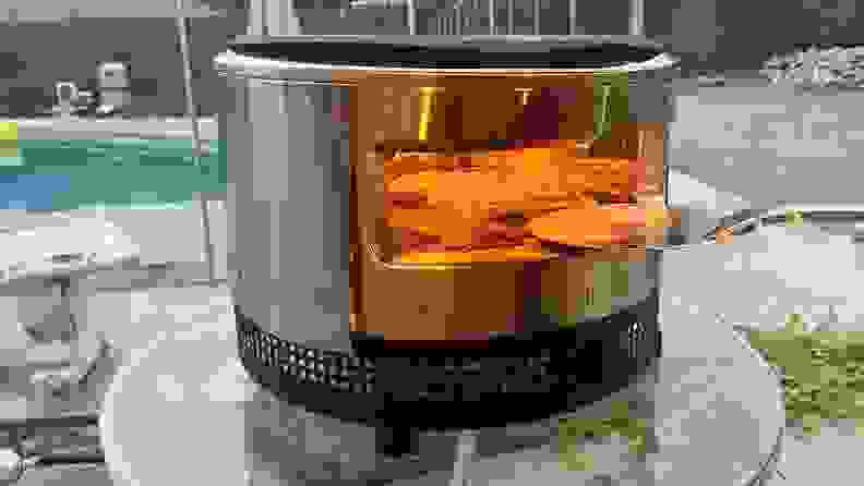 Metal pizza peel being inserted into Solo Pi Prime where pizza is cooking inside.