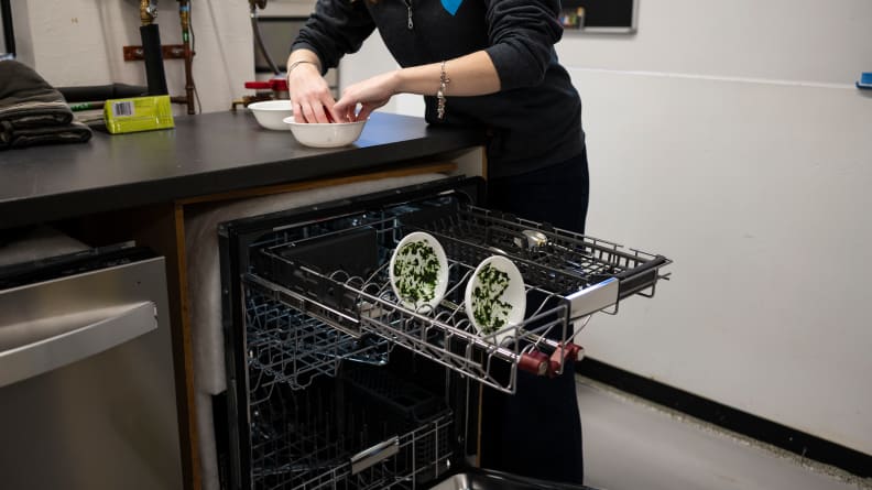 Two white bowls covered in pureed spinach sit in the top rack of a dishwasher