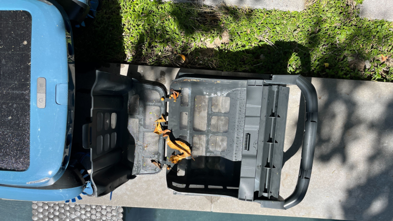 A robotic pool skimmer is open, showing leaves and debris inside