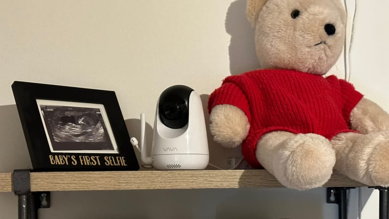 The Vava baby monitor camera fully set up on a shelf with a photograph and a stuffed teddy bear.