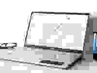 坐在白色表面上的银笔记本电脑上开放式动力，右侧有黑色杯子，左侧有一副眼镜