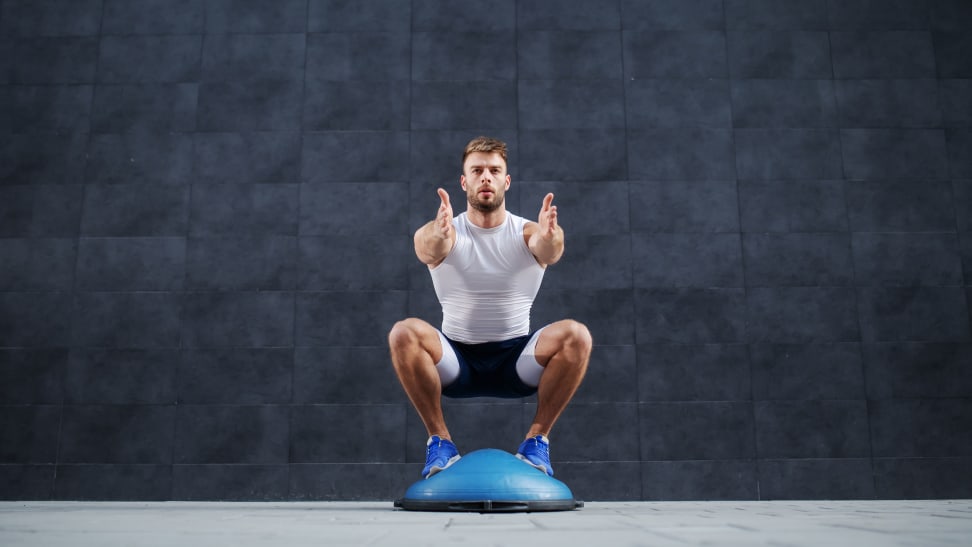 A man squatting on the rounded side of a BOSU ball.