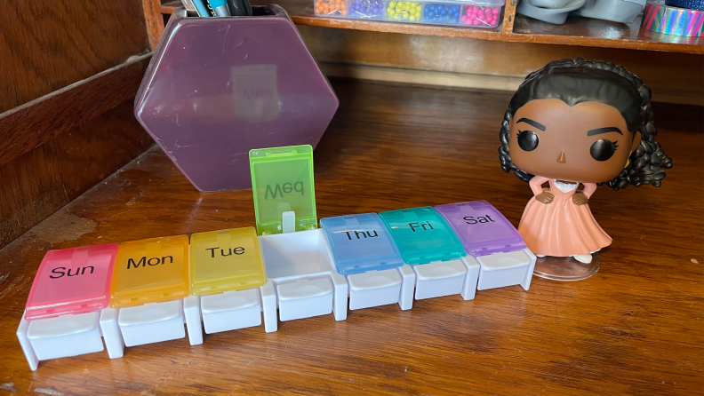 The Auvon Weekly Pill Organizer Arthritis Friendly next to a Funko Pop figurine