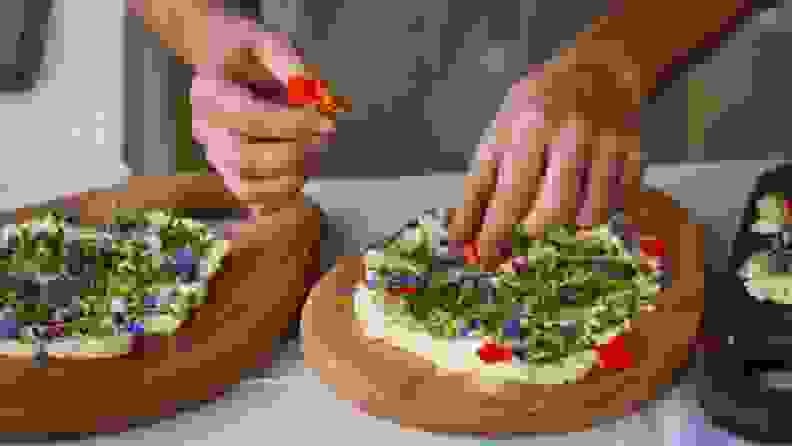 Hand placing toppings on a wooden cutting board smeared with butter