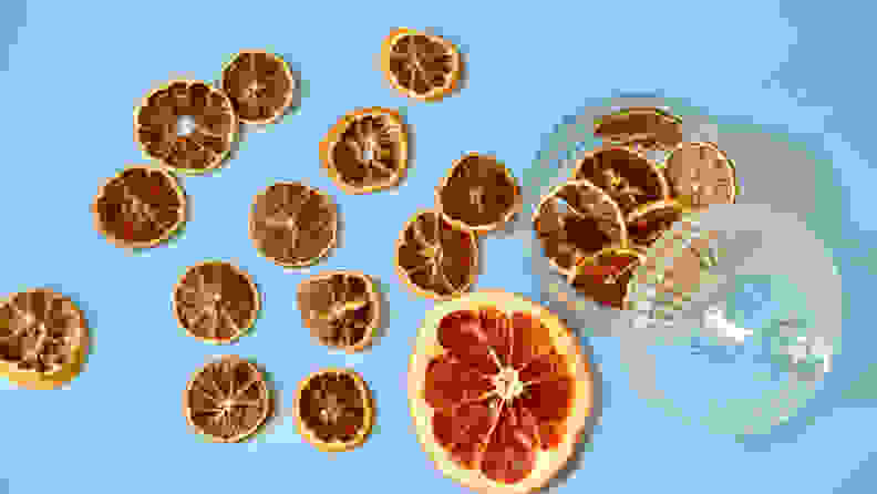 Slices of dehydrated citrus fruits are scattered around the picture and  some pieces of hydrated lime wheels are in the glass container on the right.