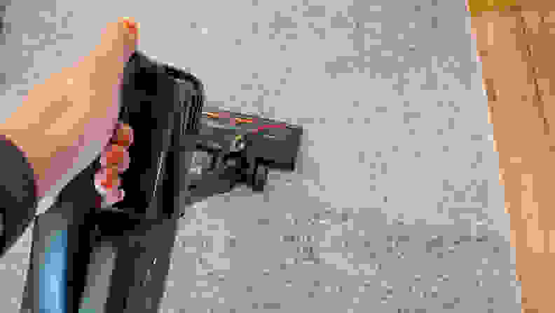 A hand holding a stick vacuum on a carpet