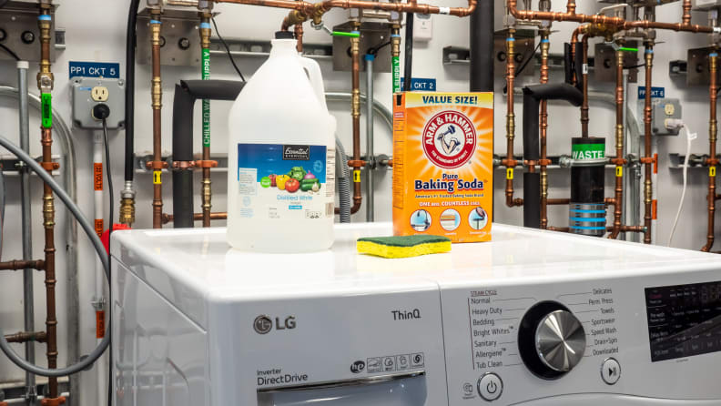 A jug of vinegar, a box of baking soda, and a sponge atop a washing machine