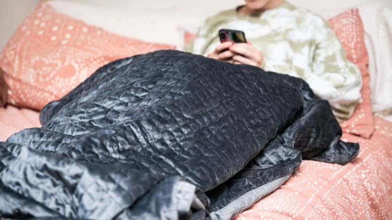 a woman sits under the gravity blanket in bed