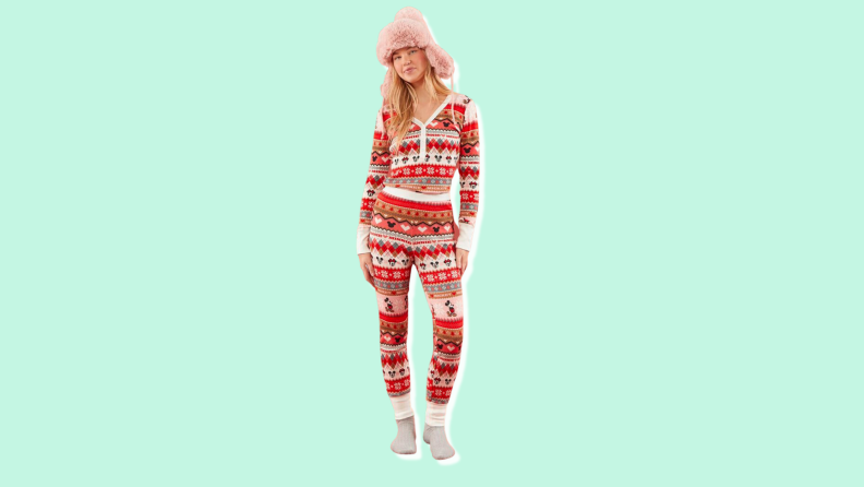 A woman wearing a furry hat stands facing the camera, wearing a red and green plaid set of long john style pajamas with a Mickey Mouse pattern.