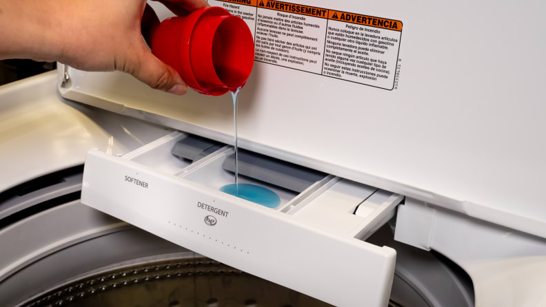 A hand reaches into frame to pour some liquid detergent into the Whirlpool Cabrio WTW7000DW detergent drawer.
