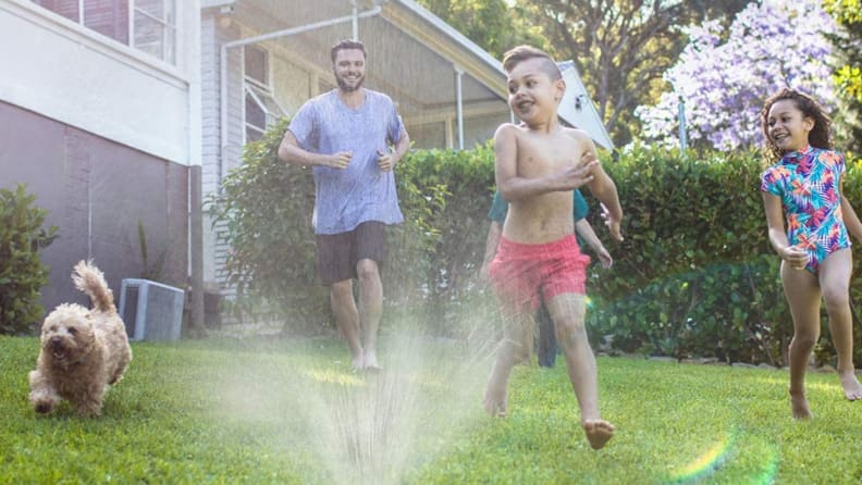A family running through a sprinkler outside.