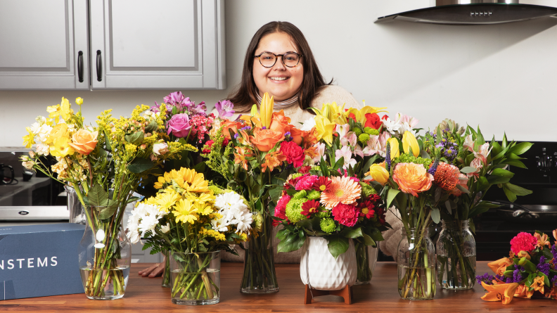 A person standing behind a variety of flower arrangements.