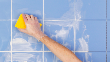 戴手套的手用海绵清洗瓷砖墙壁。