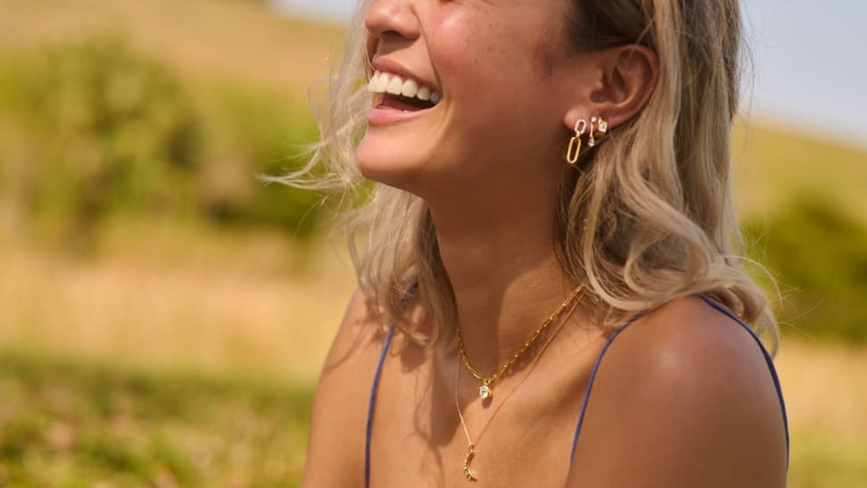 Girl smiling while wearing gold necklaces and gold earring stack