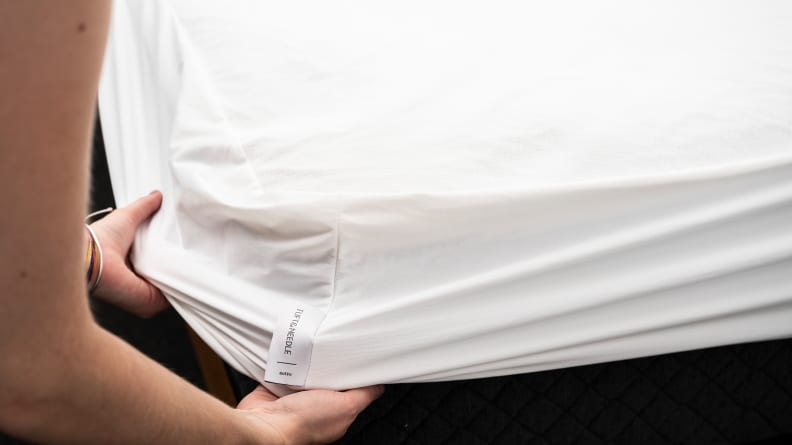 le mani tirano il proteggi-materasso Tuft & Needle sopra l'angolo di un letto