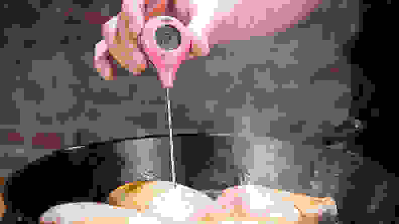 ThermoPop needle being inserted into chicken, cooking in a cast iron pan with brick wall in background.