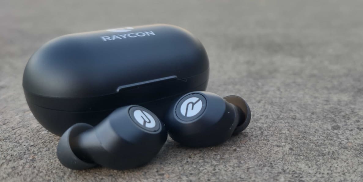 A pair of black earbuds with white highlights sit on grey pavement.