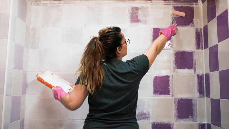 A person primes shower tiles in a bathroom before painting them.