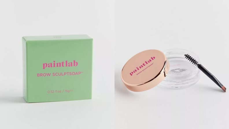 On the left: A small, light green box with pink lettering on it. On the right: A clear jar with clear brow gel in it uncapped with its gold lid and spoolie brush leaning on the jar.