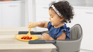 A child eats a snack at the table while seated in a Chicco clip-on high chair.