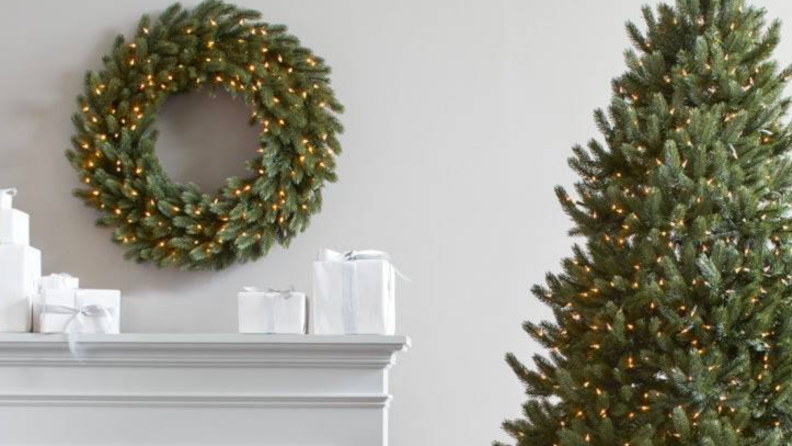 Artificial evergreen wreath over a fireplace mantle next to a Christmas tree