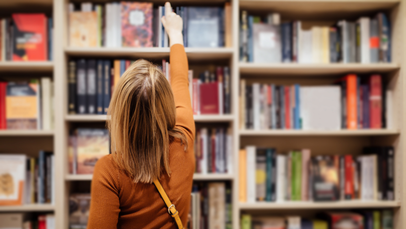 Woman in book store reaching up to the top shelf to grab a book.