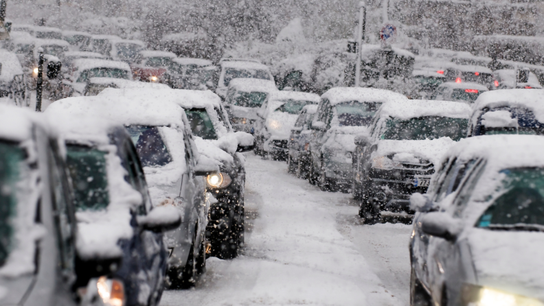 Cars covered in snow are stuck in traffic during snowstorm.