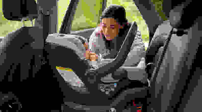 Person crouched near a baby in a car seat in the back of a cat