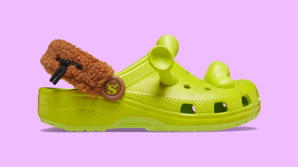 A pair of green Crocs clogs with a fuzzy brown strap and a green nose and ear Jibbitz Charms.