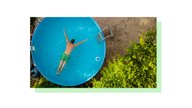 A person shown swimming in an above ground pool in a yard not yet landscaped.