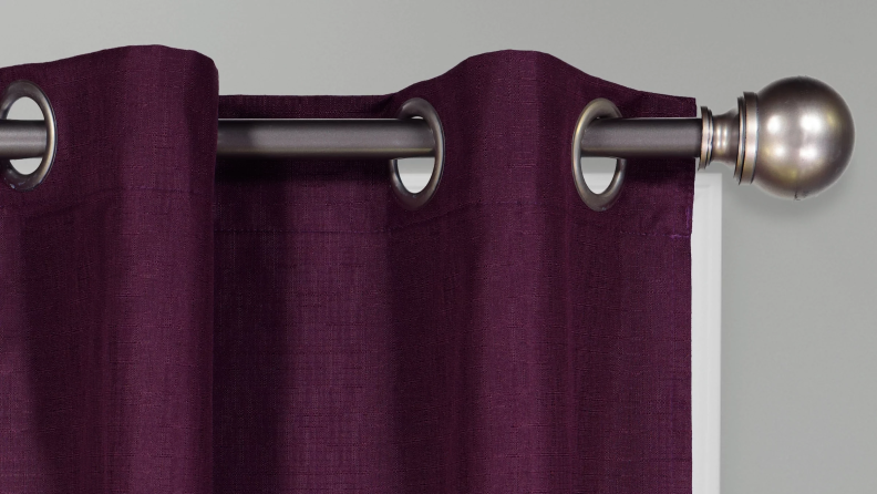 Close-up of the grommets of an Eclipse Dayton blackout curtain, hung on a metal curtain rod. The curtain itself is purple.