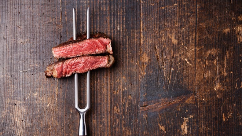 A BBQ fork holding two slices of medium rare steak
