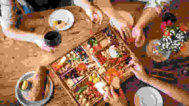 An aerial shot of the cheeseboard on a table, with wine, plates, and hands in the shot