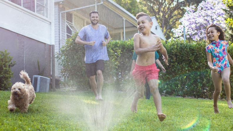 A family running through a sprinkler outside.