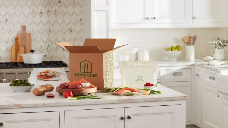 A Home Chef box sits open on a kitchen counter, surrounded by ingredients.